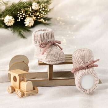 Handgestrickte Babyschuhe aus Merinowolle in Sand und Rosé auf kleinem Holzschlitten mit Holzspielzeug dekoriert
