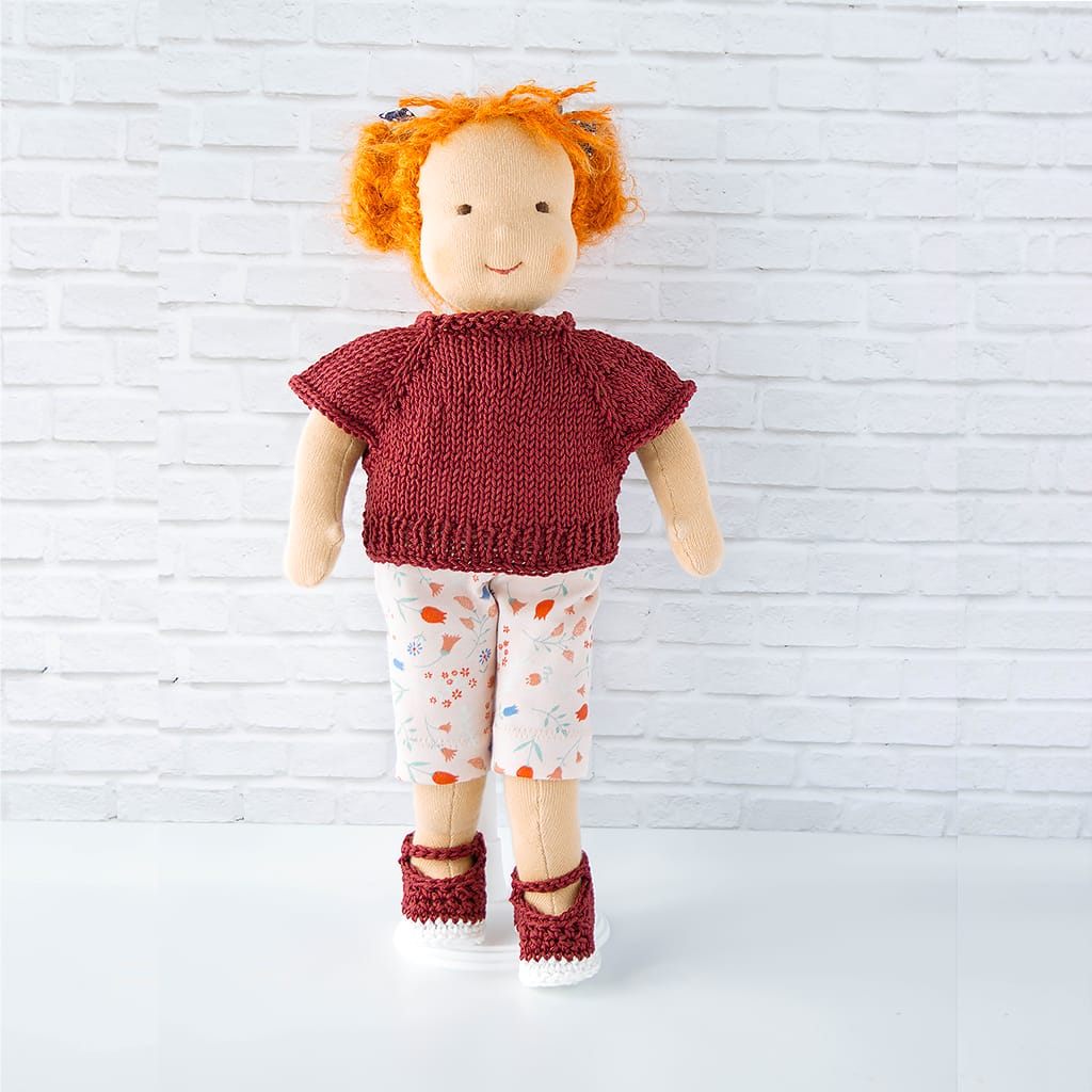 Waldorfpuppe trägt sommerliches Outfit mit handgestricktem Pullover, gemusterter Hose und passenden Schuhen