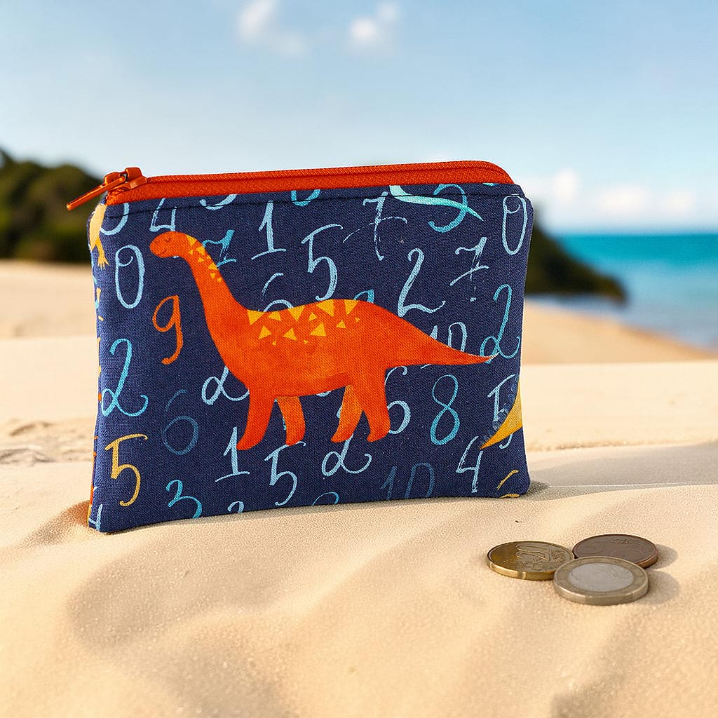 Kleine Geldbörse für Kinder mit orangefarbenem Dinosaurier und Zahlenmuster am Strand dekoriert mit Münzen