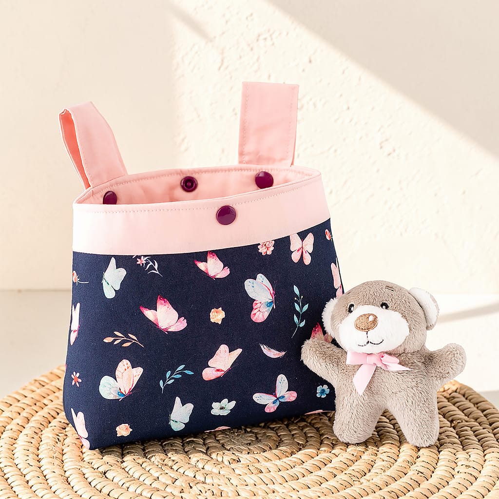 Handgemachte Lenkertasche für Kinderfahrrad mit Schmetterlingen in Rosa und Dunkelblau neben kleinem Teddybär fotografiert
