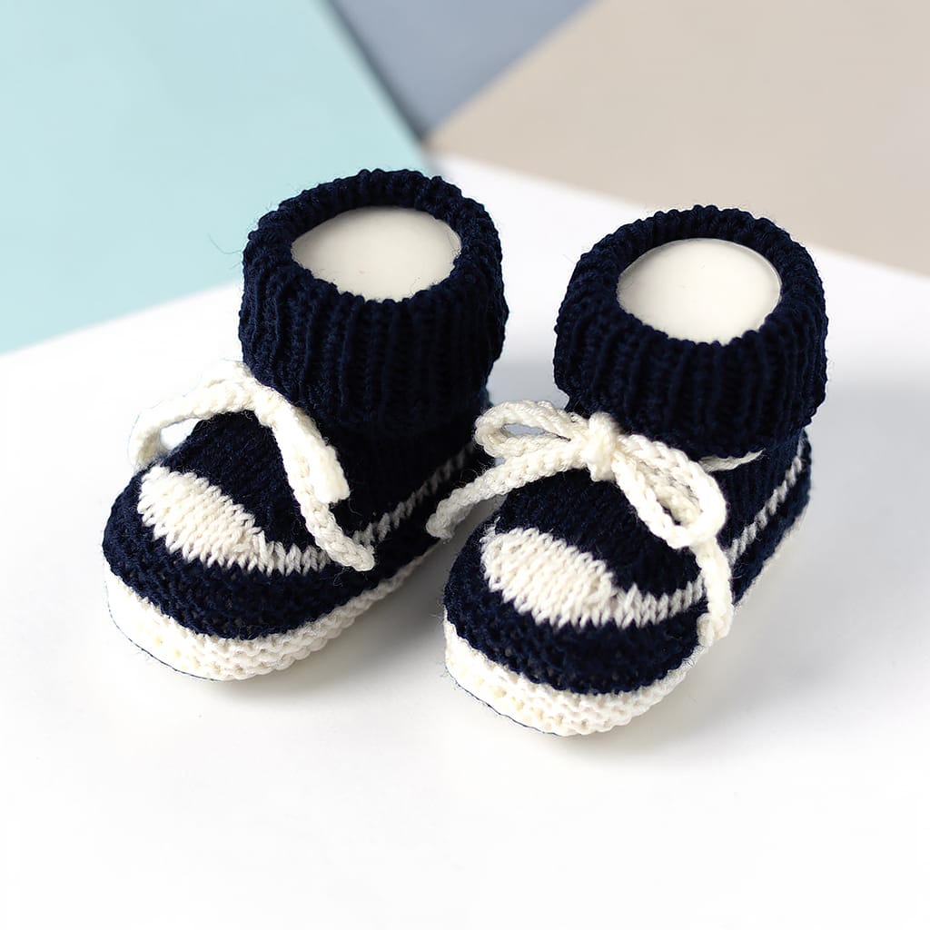Ein Paar marineblau-weiß gestreifte Baby-Booties. Die gestrickten Booties haben einen gerippten Bund und weiße Schnürsenkel, die zu einer Schleife gebunden sind. Die Sohlen und Streifen sind weiß.