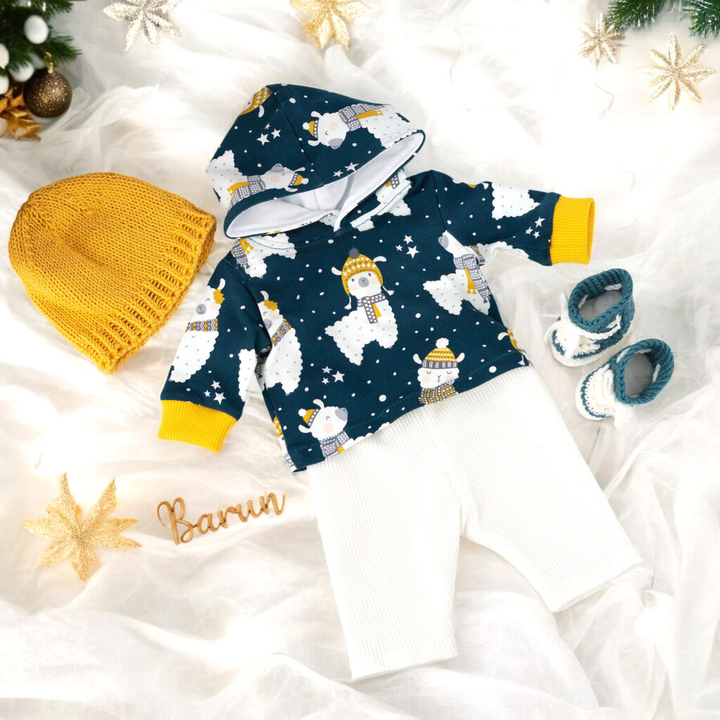 Puppenkleidungs-Set mit Lama-Motiv, Kapuzenpullover, heller Hose, gestrickter Mütze und gehäkelten Schuhen auf hellem Stoff
