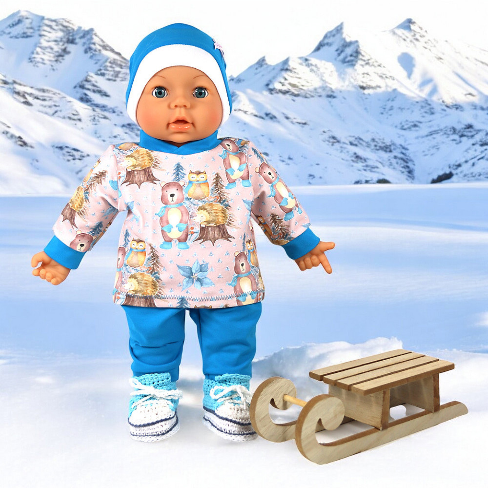 Puppenkleidung für Babypuppe 43 bis 46 cm mit Wintertier-Motiv, blauer Hose, Mütze und gehäkelten Schuhen vor winterlicher Berglandschaft