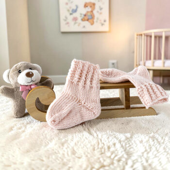 Handgestrickte Babysocken und passender Schal aus Merinowolle in Puderrosa auf Holzschlitten im Kinderzimmer