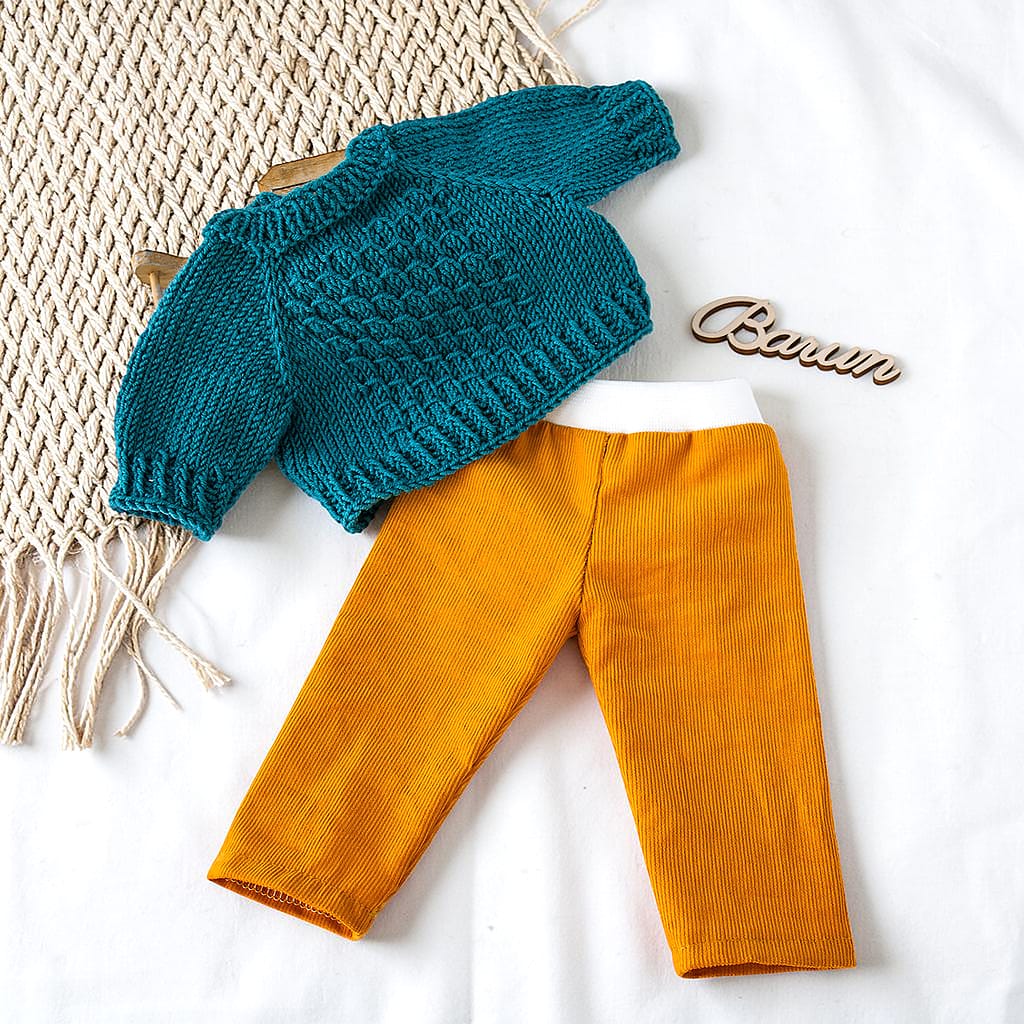 Puppenkleidung für Waldorfpuppen: senfgelbe Babycordhose kombiniert mit petrolfarbenem handgestricktem Puppenpullover auf hellem Stoffhintergrund.