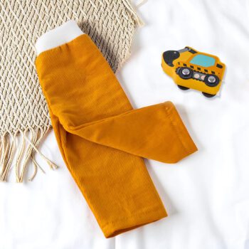 Senfgelbe Puppenhose aus Babycord für Waldorfpuppen, fotografiert auf hellem Stoff mit Flechtmatte und kleinem Holzbagger. Elastischer Bund und bequeme Passform für Puppen von 38 cm