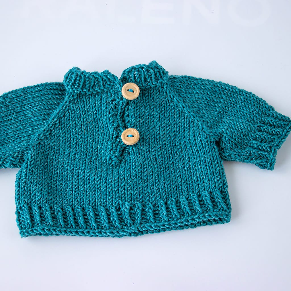 Rückseite eines handgestrickten Puppenpullovers aus Merinowolle mit Knopfverschluss im Nackenbereich.