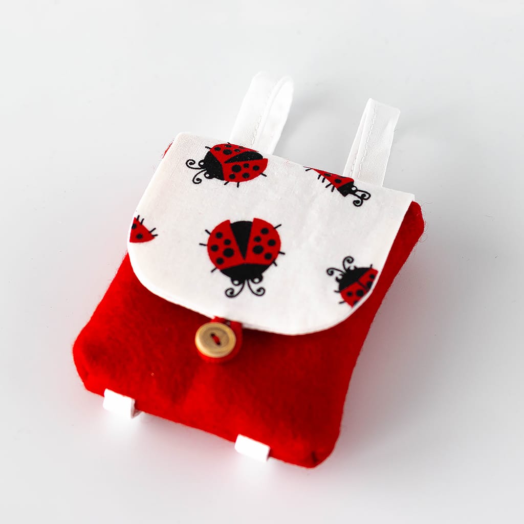 Kleiner Puppenrucksack aus rotem Wollfilz mit weißer Klappe im Marienkäfer-Design und verstellbaren Trägern für Puppen von 38 cm