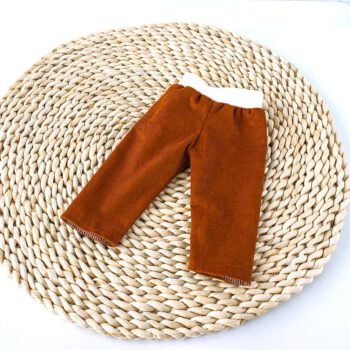 Rostbraune Puppenhose aus feinem Cord mit weichem weißem Bündchen für Puppen von 36–38 cm auf geflochtener Naturunterlage.