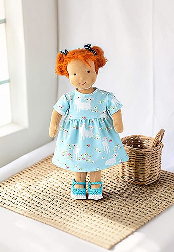 Waldorfpuppe trägt blaues Kleid mit kleinen Schäfchen