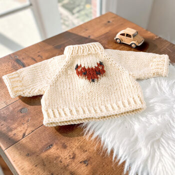 Handgestrickter naturfarbener Puppenpullover aus Merinowolle mit aufgesticktem Fuchskopf für Puppen von 36–40 cm, dekoriert auf einem Holztisch mit kleinem Holzauto.