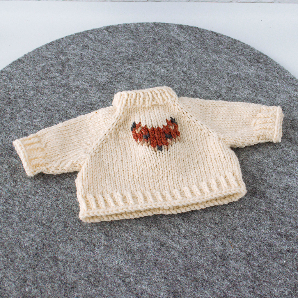 Handgestrickter Puppenpullover aus naturfarbener Merinowolle mit aufgesticktem Fuchskopf auf grauem Filzuntergrund, passend für Puppen von 36–40 cm.