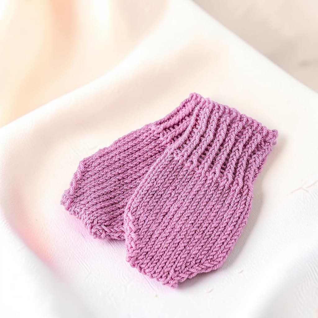 Zwei gestrickte Babyhandschuhe in Altrosa mit unterschiedlichen Strickmustern und geripptem Abschluss