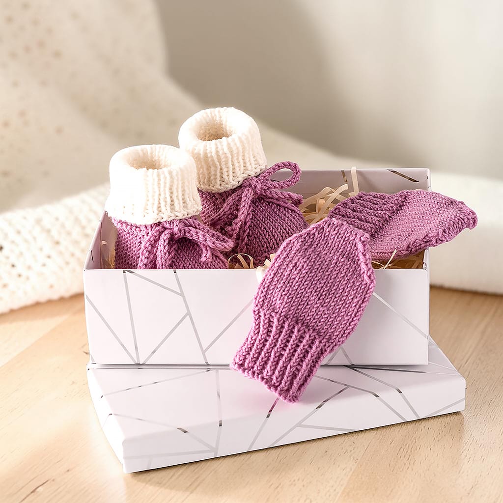 Gestricktes Babyset in Altrosa und Creme als Geschenk in einer weißen Geschenkbox mit Linienmuster