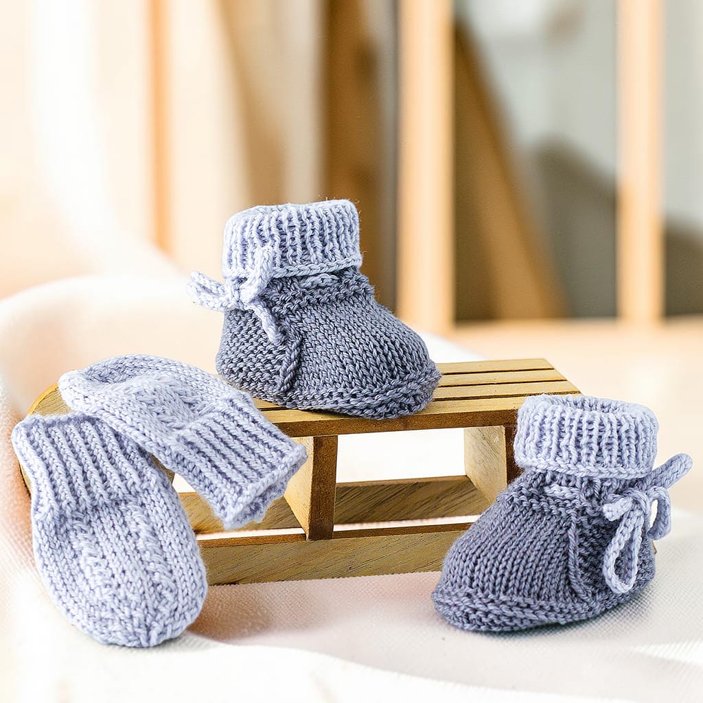 Gestricktes Babyset aus Merinowolle und Kaschmir mit Babyschuhen und Fäustlingen auf einem Holzschlitten