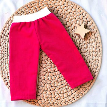 Pinke Babycordhose für eine Waldorfpuppe, flach auf einer runden Flechtmatte ausgelegt