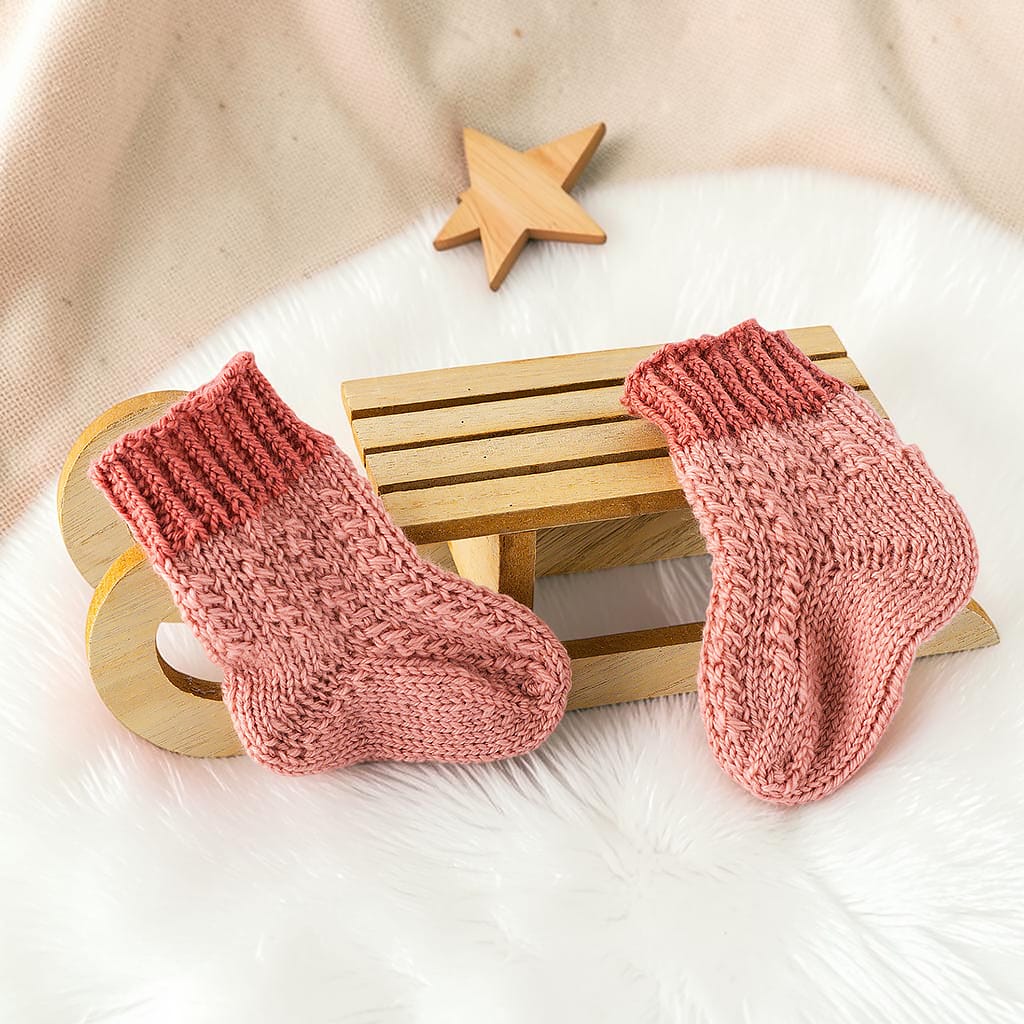 Zwei gestrickte Babysocken für Neugeborene in warmem Altrosa mit geripptem Bündchen